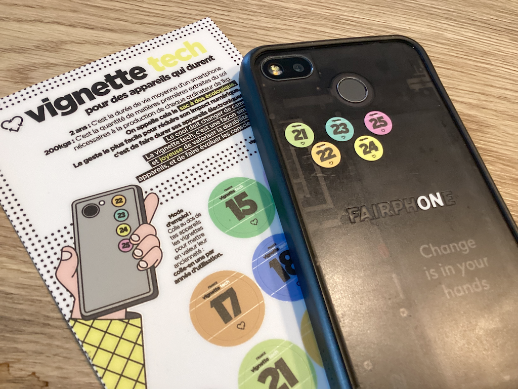 Planches de vignettes et smartphone (Fairphone 3) posé à l'envers sur une table. Sur le smartphone, les vignettes de 21 à 25 sont collées.