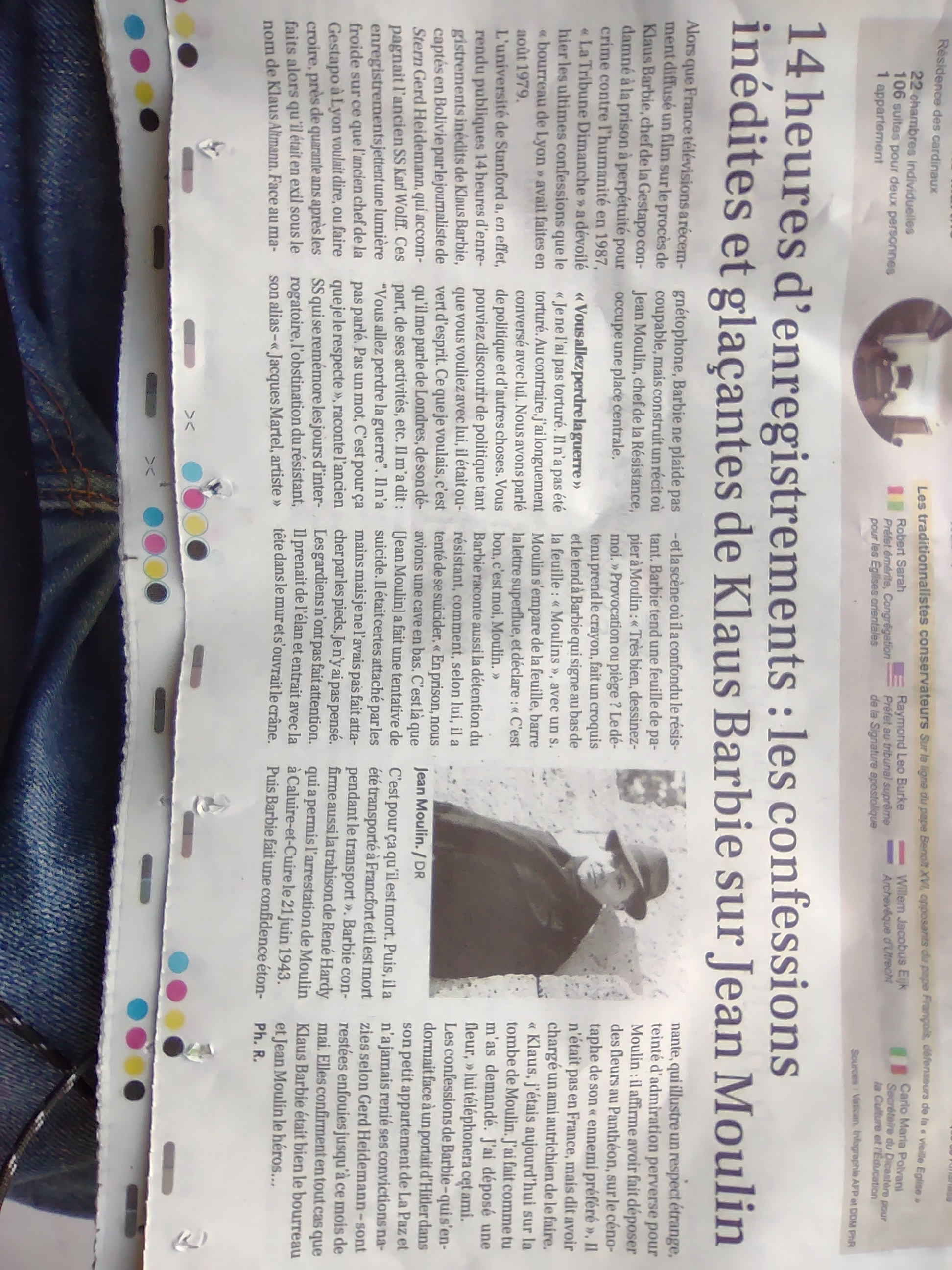 Une image prise au smartphone d'un article qui occupe le tiers bas d'un journal en papier. Le titre: "14 heures d'enregistrements : les confessions inedites et glacantes de Klaus Barbie sur Jean Moulin". L'article est aussi accompagné d'un portrait photo de Jean Moulin en noir et blanc, présumément avant sa mort dans les années 1930 ou 40.